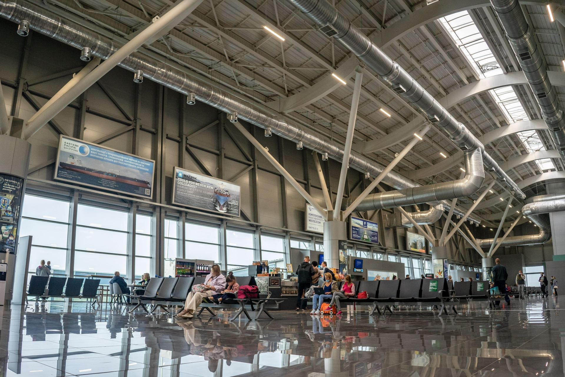 A spacious airport terminal with travellers waiting by the windows