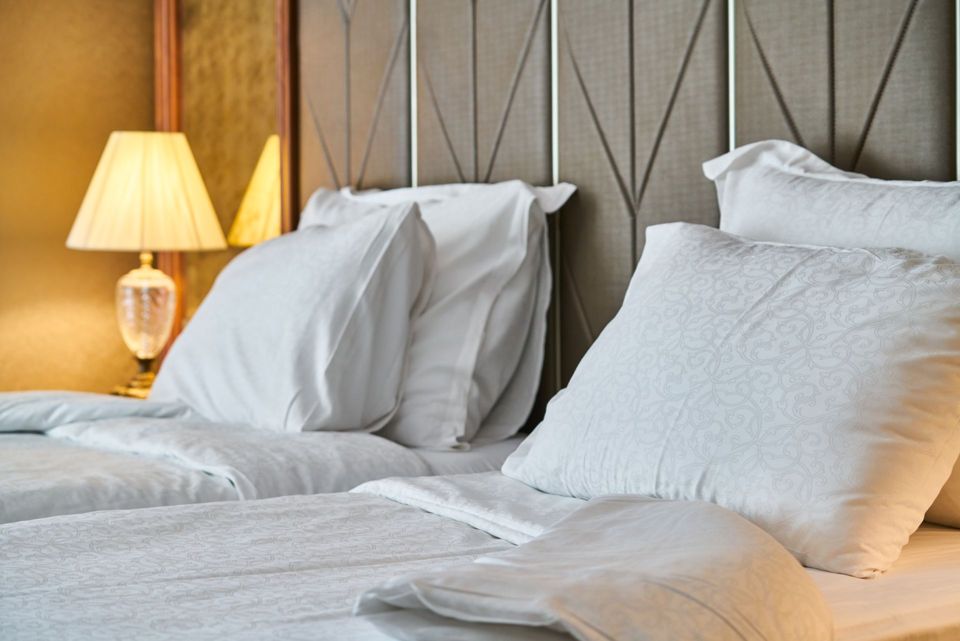 A made-up hotel bed with white pillows and warm bedside lamps